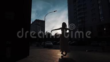 芭蕾舞演员的剪影，穿着飞行服装在户外跳舞。 苗条的女孩在城市建筑的背景下跳舞。
